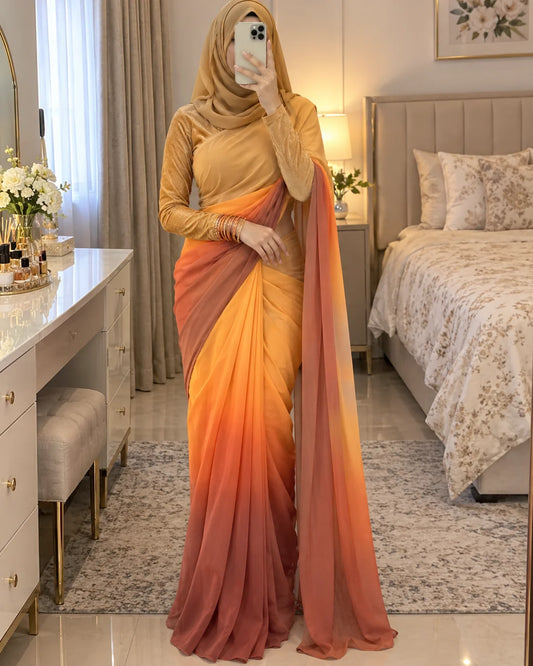 A woman wearing a long-sleeve mustard yellow top and a draped gradient sari in shades of orange, yellow, and dusty rose, standing in a bedroom taking a mirror selfie.