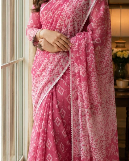 Woman in pink batik print saree standing by window, full drape