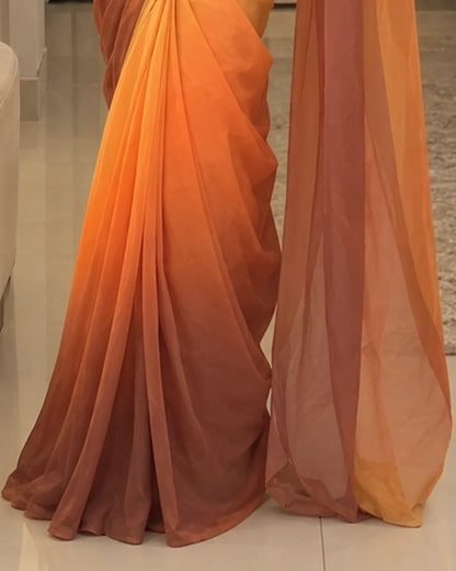 Two draped chiffon sarees with a warm ombre gradient transitioning from bright orange at the top to terracotta and rust at the bottom, displayed on a light-colored floor.