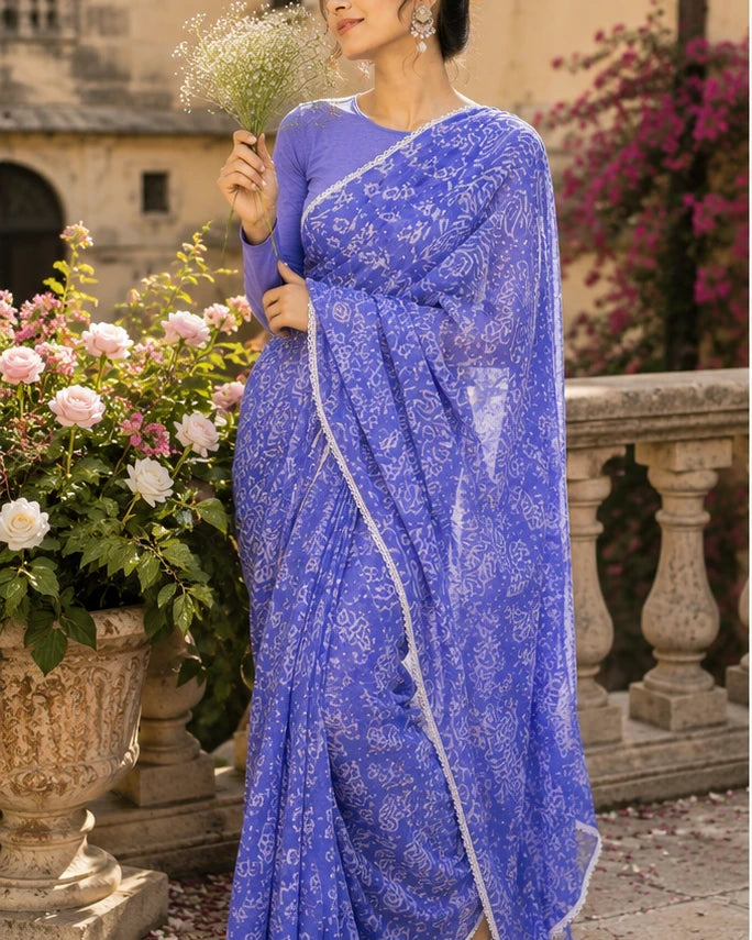 Woman in periwinkle blue batik print saree holding flowers in courtyard garden