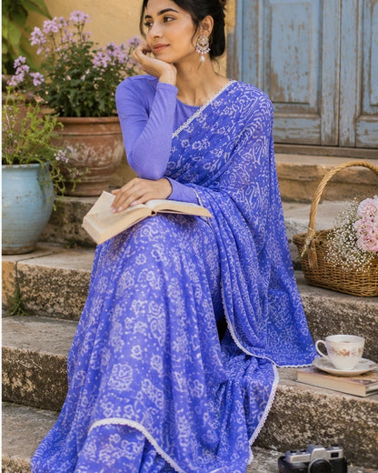Woman in periwinkle blue batik print saree seated on stone steps with book