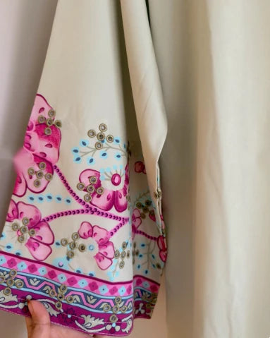 Close-up of magenta floral embroidery on sage green sleeve border